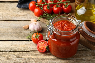 Photo of Homemade tomato sauce in jar and ingredients on wooden table. Space for text