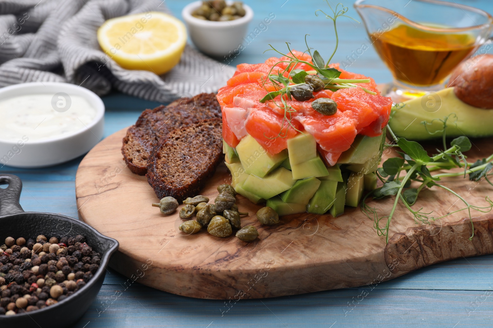 Photo of Delicious salmon tartare with avocado and croutons on light blue wooden table