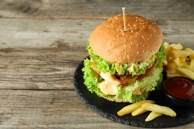 Photo of Burger with delicious patty, french fries and sauce on wooden table, space for text