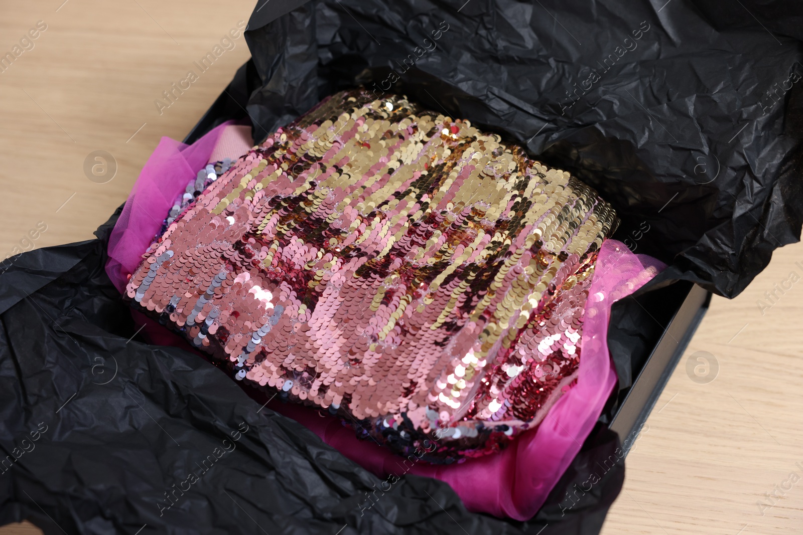 Photo of Stylish pink carnival costume with sequins in black box on wooden table, closeup