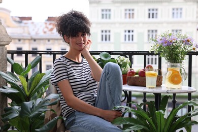 Photo of Young woman relaxing at table on balcony with beautiful houseplants