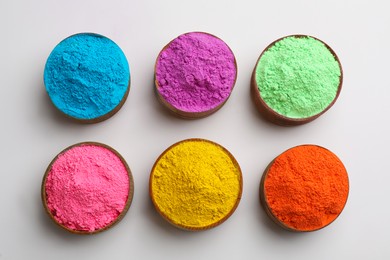 Photo of Colorful powders in bowls on light background, flat lay. Holi festival celebration