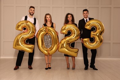 Happy friends with golden 2023 balloons indoors. New Year celebration