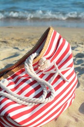 Photo of Stylish striped bag with dry starfish on sandy beach near sea