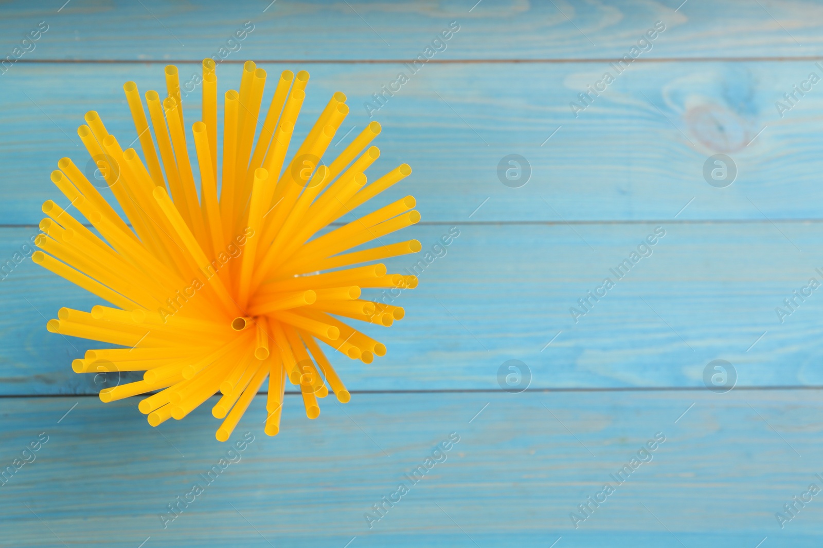 Photo of Yellow plastic drinking straws on light blue wooden table, top view. Space for text