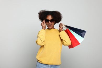 Photo of Happy African American woman in sunglasses with shopping bags on light grey background