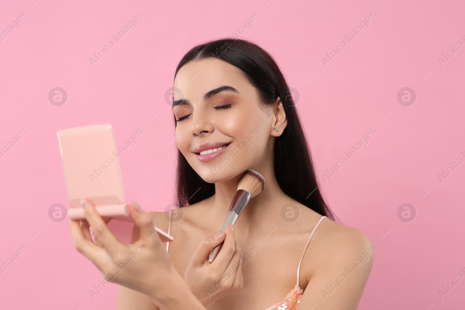 Photo of Beautiful woman with cosmetic pocket mirror applying makeup on pink background