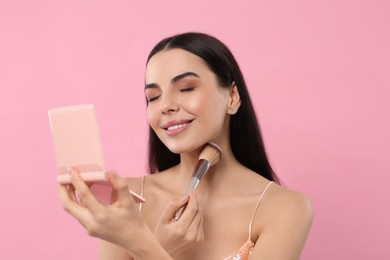 Beautiful woman with cosmetic pocket mirror applying makeup on pink background