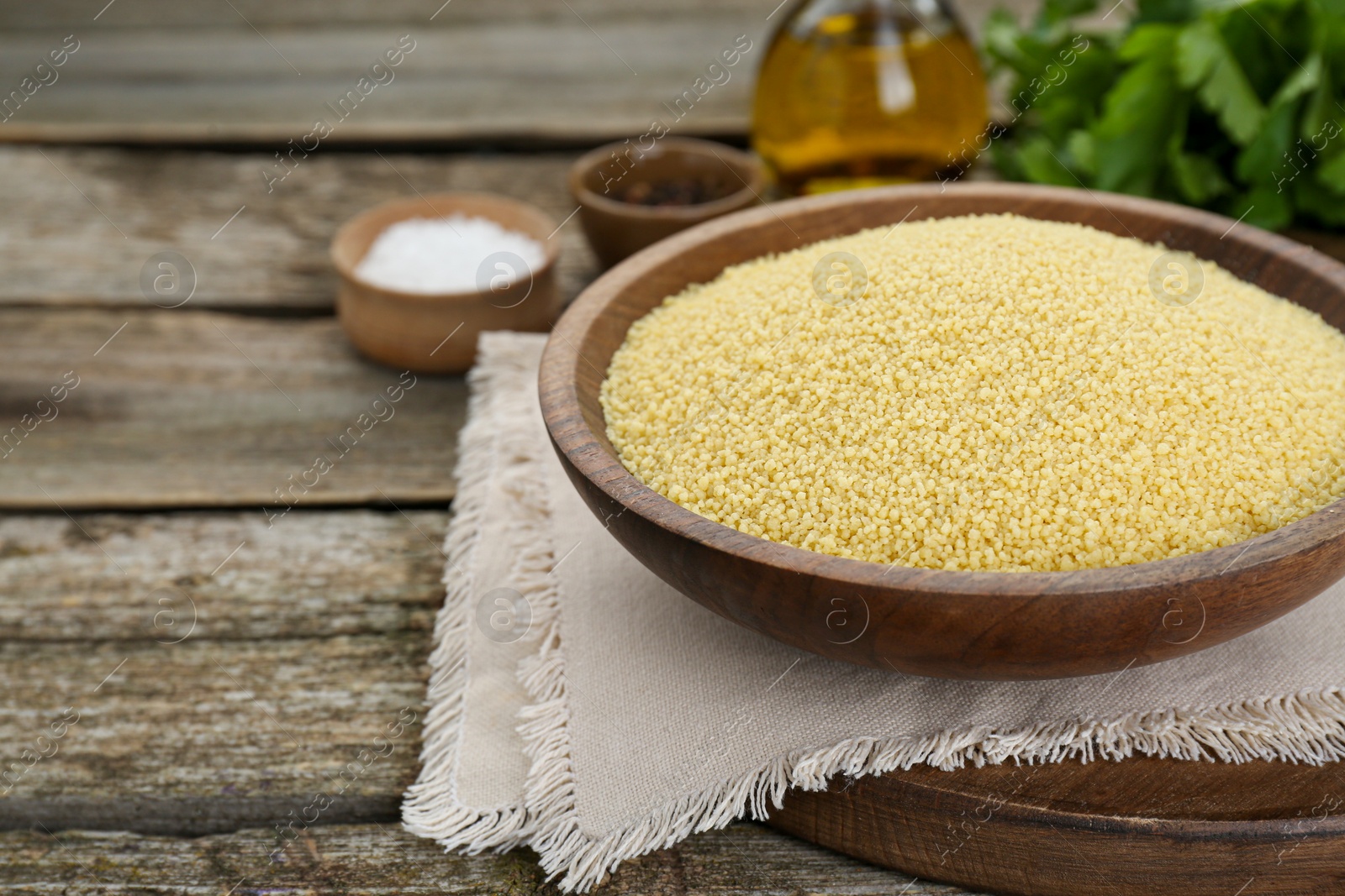 Photo of Bowl of raw couscous on wooden table, closeup. Space for text