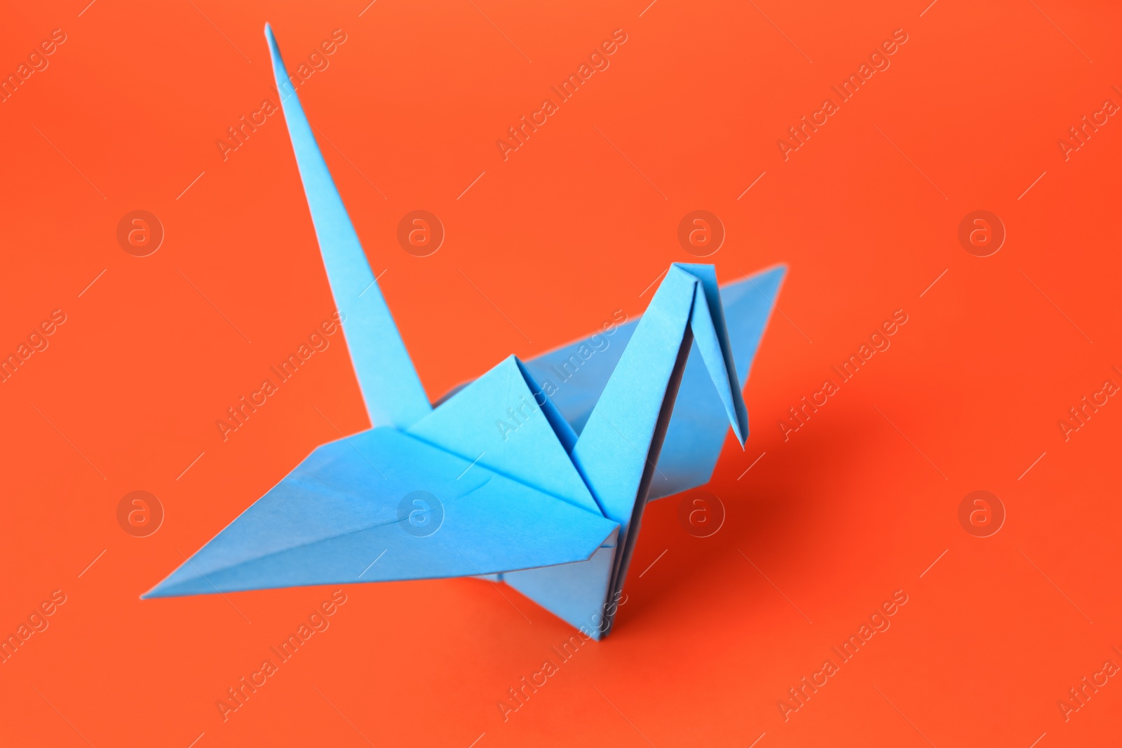 Photo of Origami art. Handmade paper crane on orange background, closeup