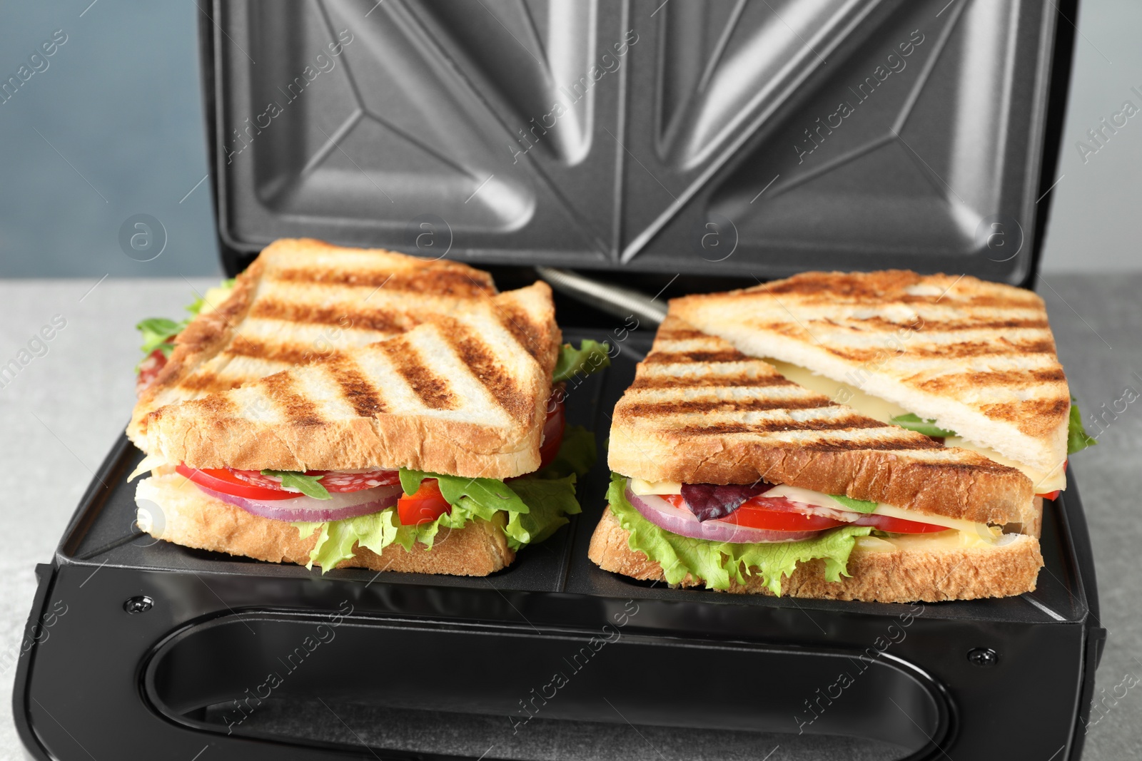 Photo of Modern grill maker with sandwiches on table, closeup view