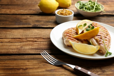 Tasty grilled chicken fillets with green sprouts and lemon slices on wooden table. Space for text