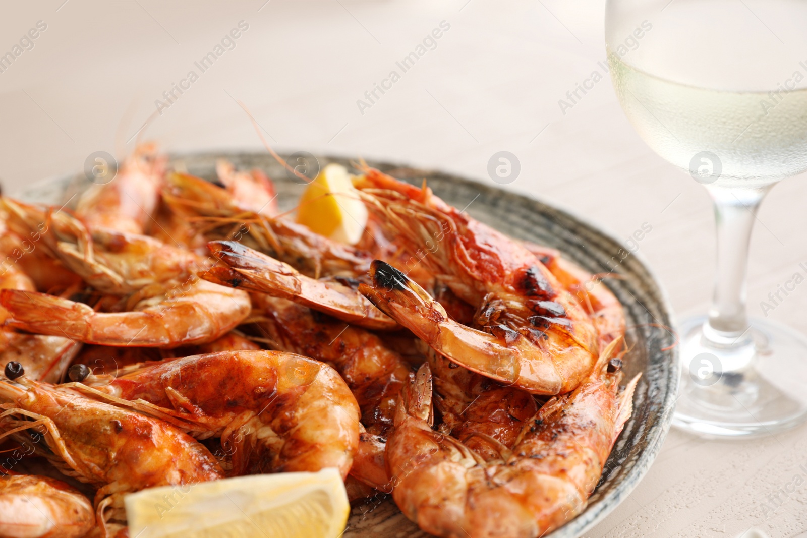 Photo of Plate of delicious cooked shrimps served with lemon and wine at table, closeup