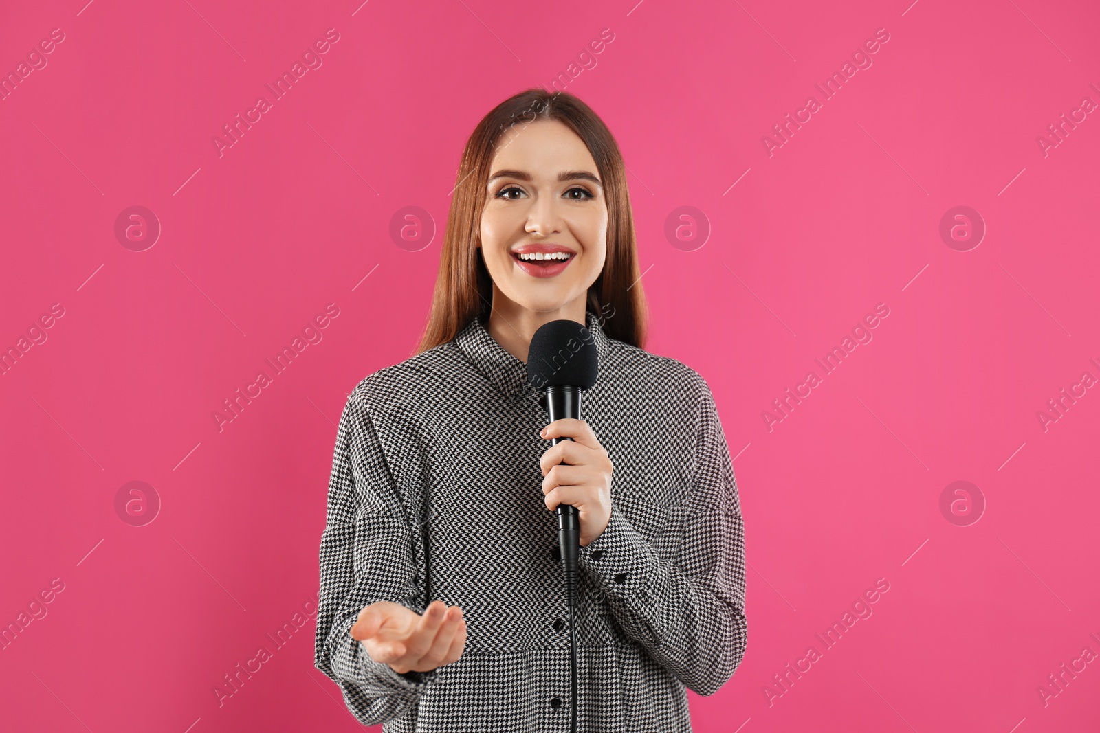 Photo of Young female journalist with microphone on pink background