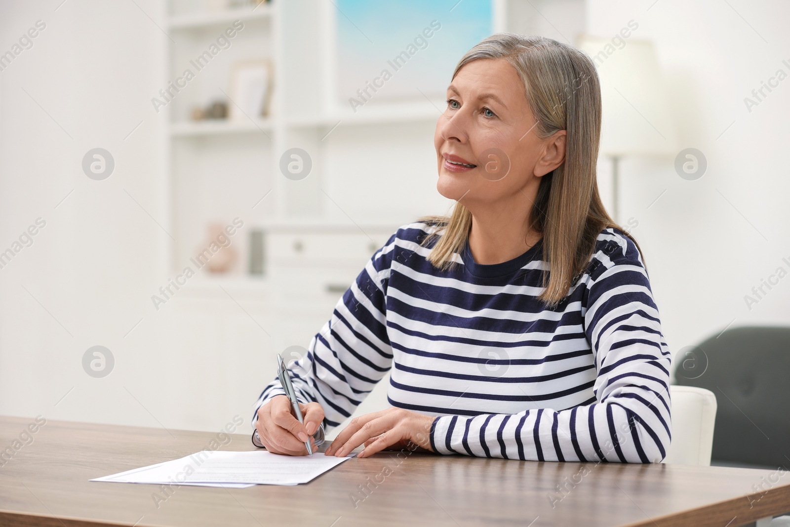 Photo of Senior woman signing Last Will and Testament at wooden table indoors. Space for text