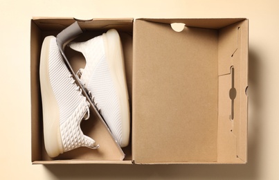 Pair of stylish sport shoes in box on beige background, top view