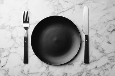 Stylish ceramic plate and cutlery on marble background, flat lay