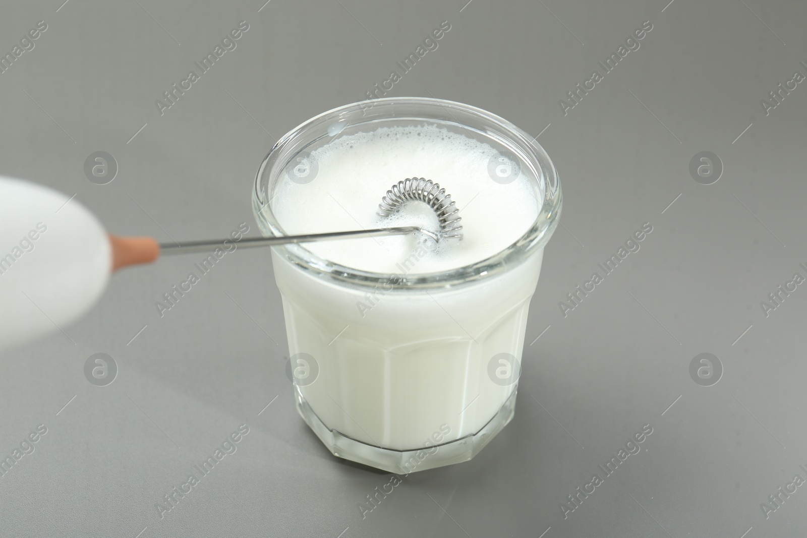 Photo of Whisking milk in glass with mini mixer (milk frother) on grey background, closeup