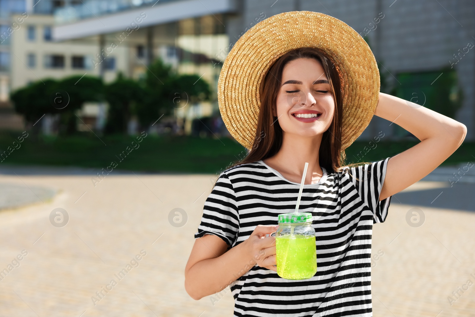 Photo of Young woman in straw hat with plastic cup of fresh juice outdoors, space for text