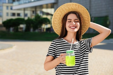 Photo of Young woman in straw hat with plastic cup of fresh juice outdoors, space for text