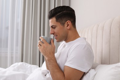 Happy man with cup of hot drink in bed at home