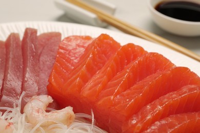 Photo of Tasty salmon slices, shrimp, funchosa and tuna on plate, closeup. Delicious sashimi dish