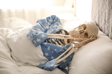 Human skeleton in pajamas lying on bed indoors