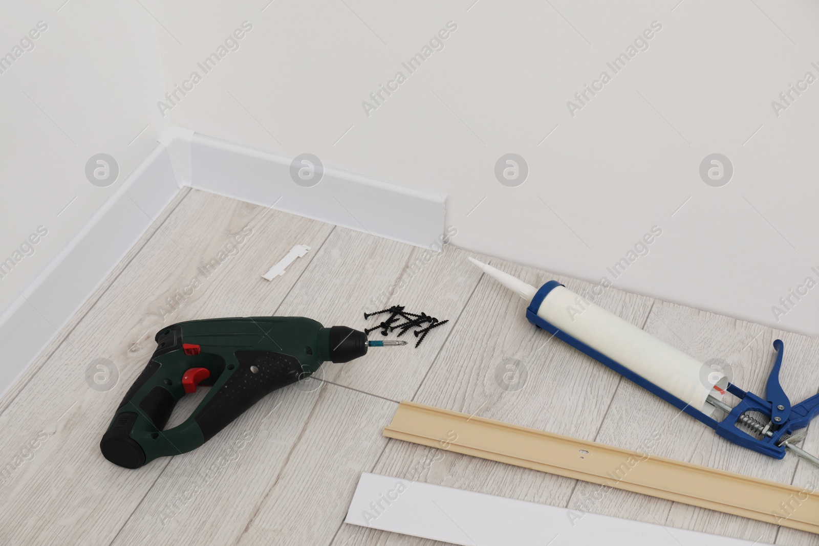 Photo of Plinths, caulking gun, screwdriver and screws on laminated floor in room