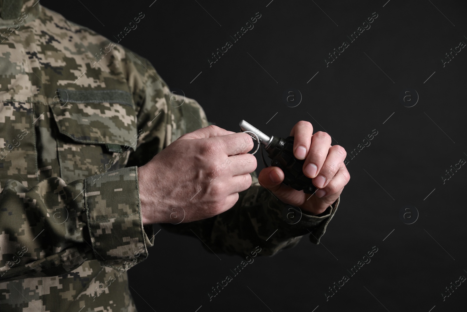 Photo of Soldier pulling safety pin out of hand grenade on black background, closeup. Military service