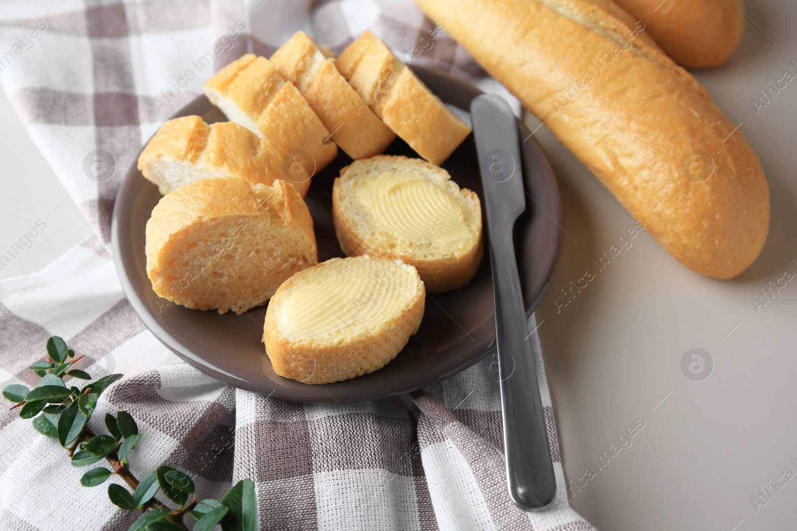 Photo of Whole and cut baguettes with fresh butter on table