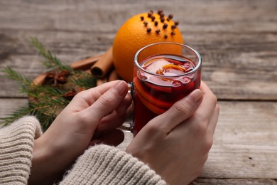 Photo of Woman with glass cup of aromatic mulled wine at wooden table, closeup