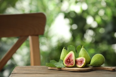 Cut and whole green figs on wooden table against blurred background, space for text