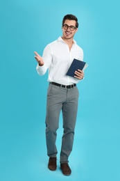 Photo of Young male teacher with glasses and notebooks on light blue background