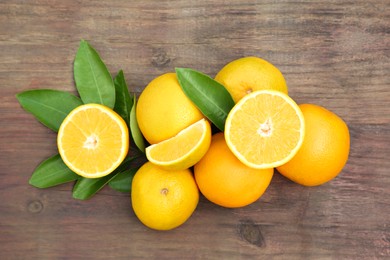 Photo of Many ripe oranges and green leaves on wooden table, flat lay