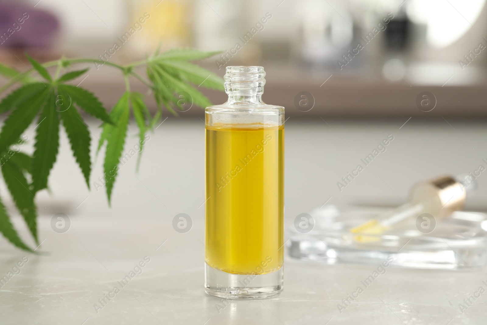 Photo of Bottle of hemp oil on light table against blurred background