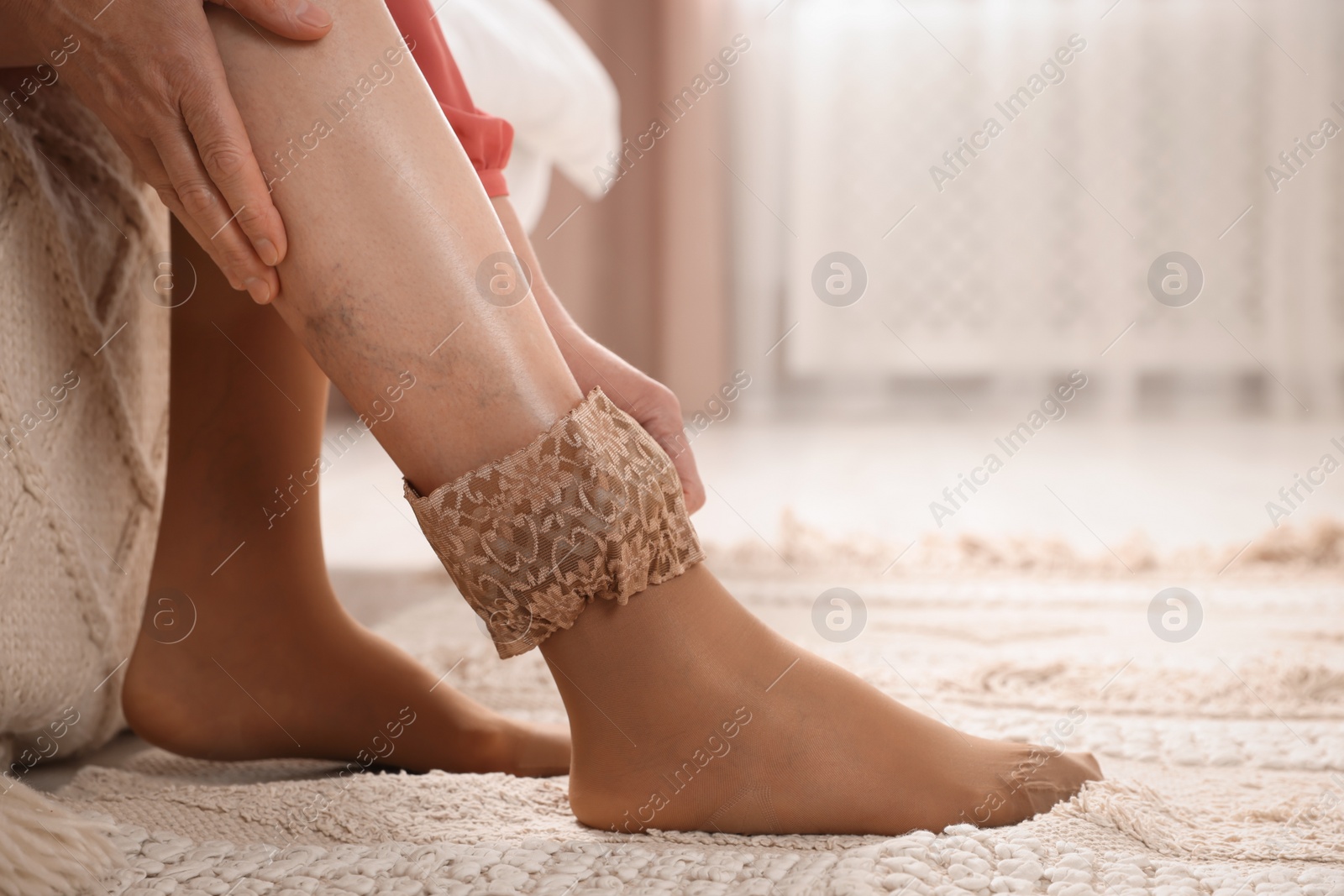 Photo of Woman putting on compression stocking in bedroom, closeup. Prevention of varicose veins