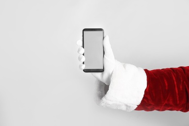 Photo of Santa holding modern mobile phone with blank screen on light grey background, closeup. Space for text