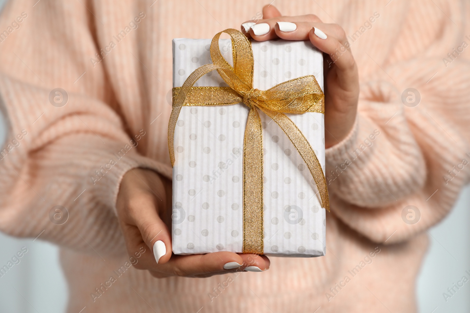 Photo of Woman in warm sweater holding Christmas gift on light background, closeup
