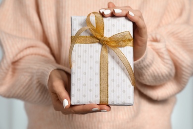 Woman in warm sweater holding Christmas gift on light background, closeup