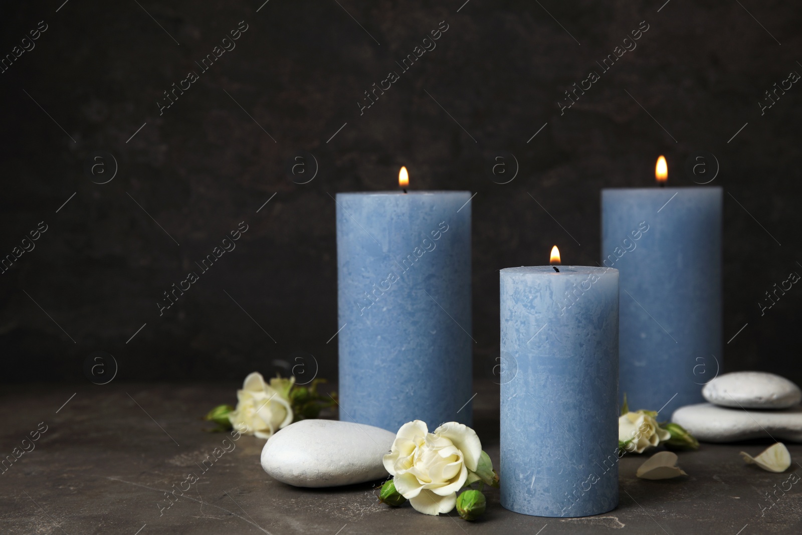 Photo of Burning candles, spa stones and flowers on dark grey table, space for text