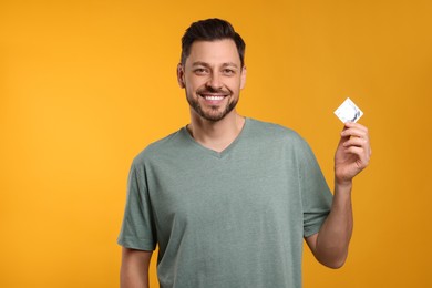 Photo of Happy man holding condom on orange background