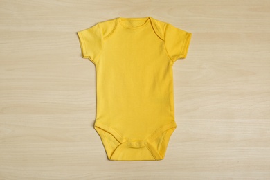 Cute baby onesie on wooden background, top view