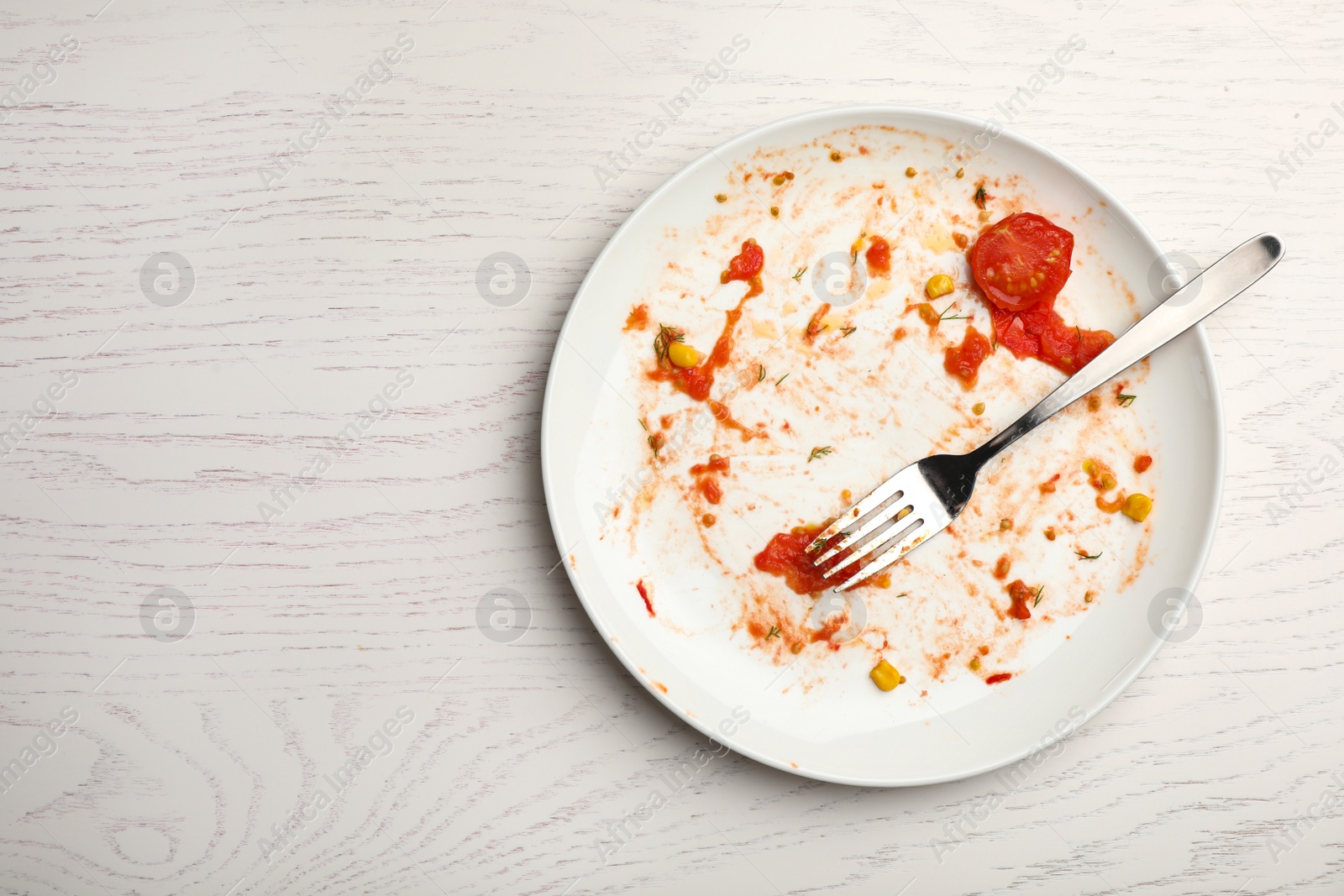 Photo of Dirty plate with food leftovers and fork on white wooden background, top view. Space for text