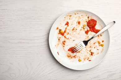 Photo of Dirty plate with food leftovers and fork on white wooden background, top view. Space for text