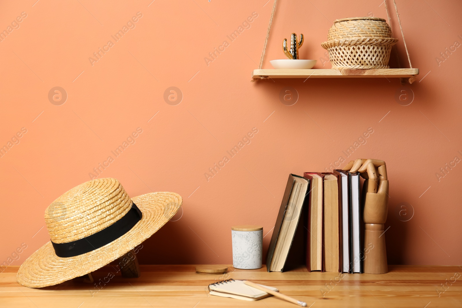 Photo of Books and straw hat on wooden table near brown wall. Interior design