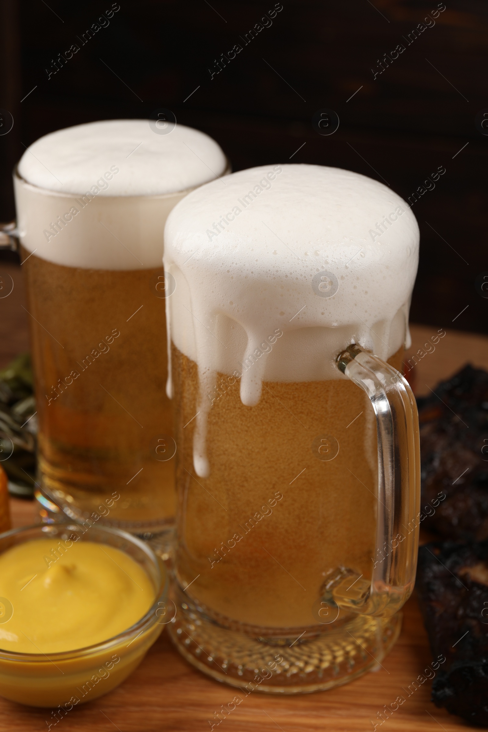 Photo of Mugs of tasty beer, meat and sauce on wooden table, closeup