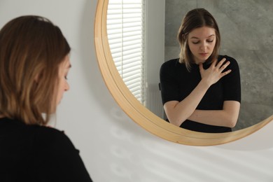 Sad young woman near mirror in room