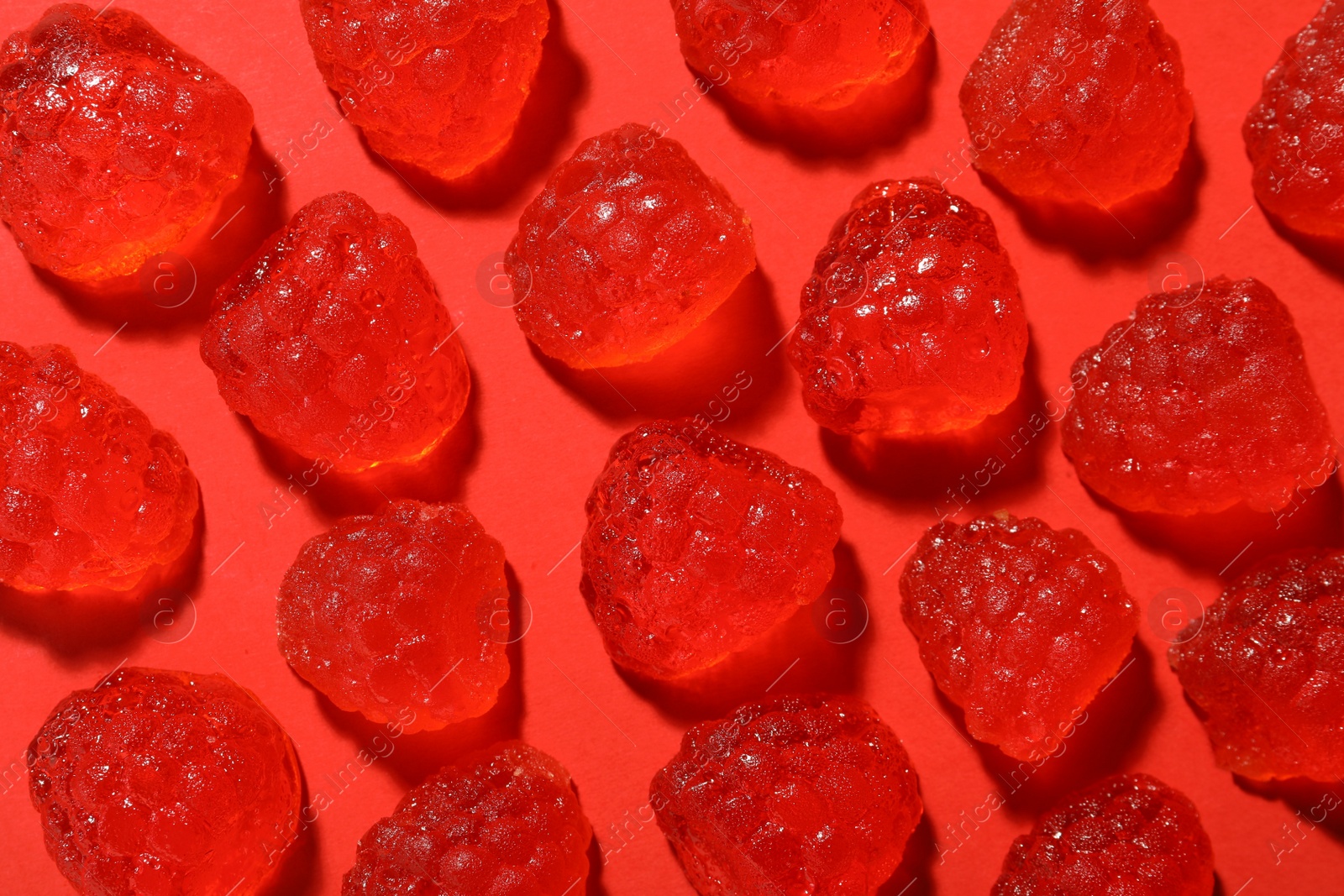 Photo of Delicious gummy raspberry candies on red background, flat lay