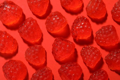 Photo of Delicious gummy raspberry candies on red background, flat lay