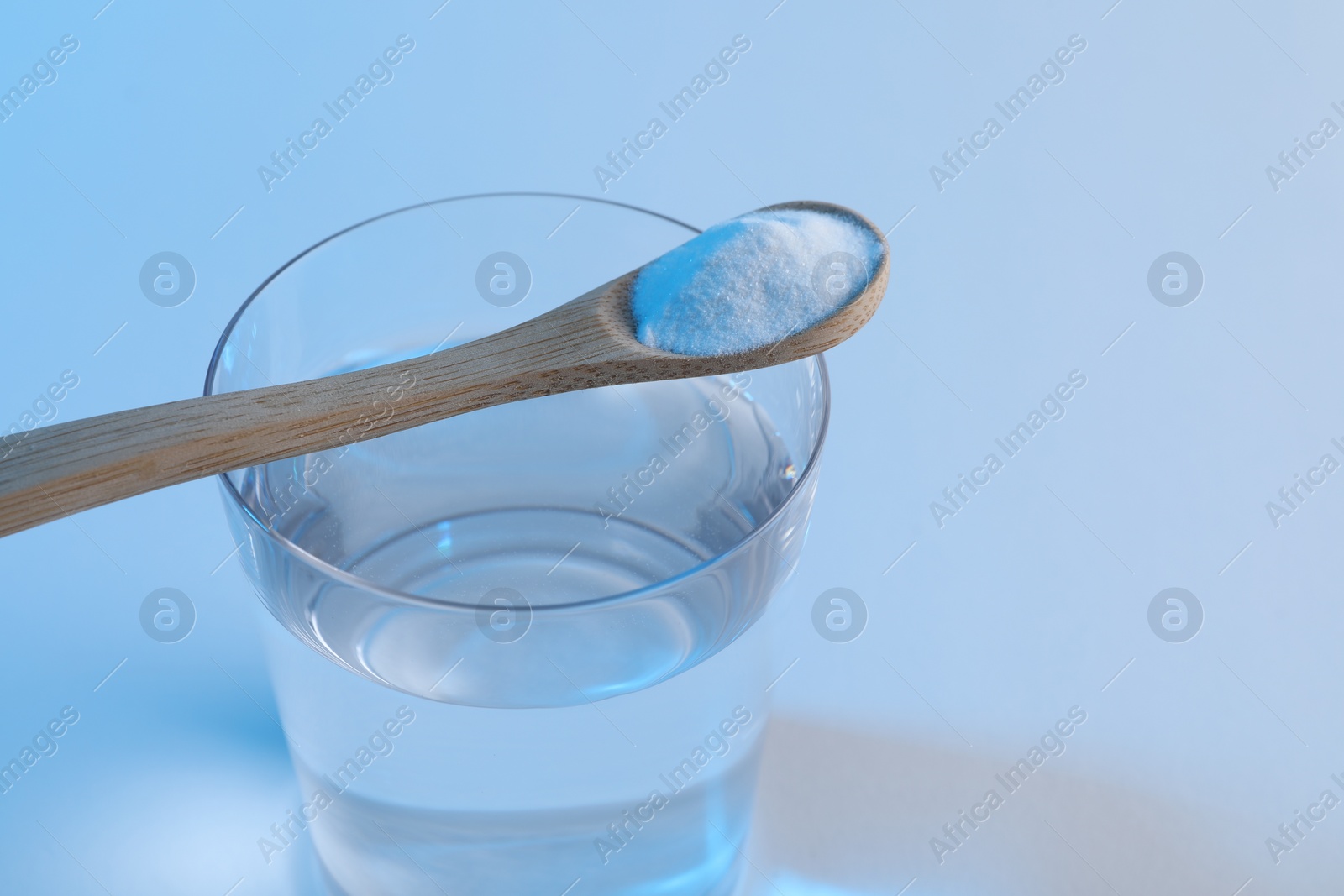 Photo of Glass of water and spoon with baking soda on light blue background, closeup. Space for text